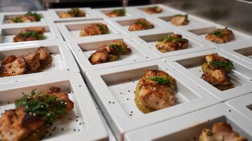 Eine Vielzahl von kleinen Gerichten auf weißen Tellern. Jedes Gericht enthält gegrilltes Fleisch und ist mit frischen Kräutern garniert.