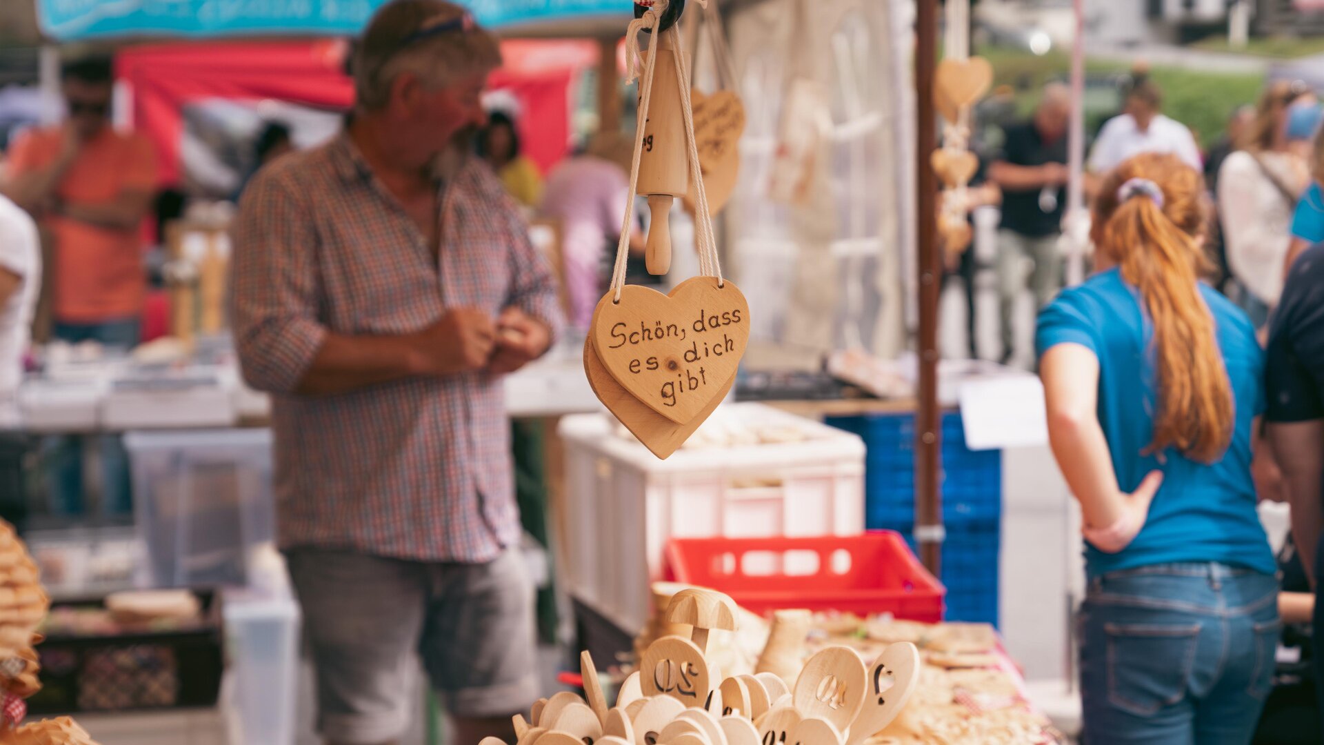 Ein Marktstand mit handgefertigten Holzartikeln. Im Hintergrund sind Menschen zu sehen, die das Angebot betrachten.