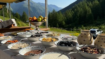 A table set with various bowls full of ingredients in nature. The mountains and the clear sky in the background create a cozy atmosphere.