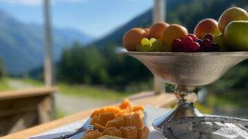 Ein schöner Ausblick auf die Berge mit frischem Obst auf einem Tisch. Im Vordergrund sind geschnittene Früchte und eine Schale mit mehr Obst zu sehen.