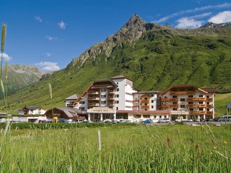 Ein schönes Hotel in den Bergen mit grünen Wiesen und blauen Himmel. Die umliegende Landschaft ist malerisch und einladend.