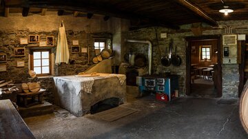 Ein rustikaler Raum mit Steinen und Holz, der traditionelles Handwerk zeigt. Es sind Werkzeuge und alte Fotografien an den Wänden zu sehen.