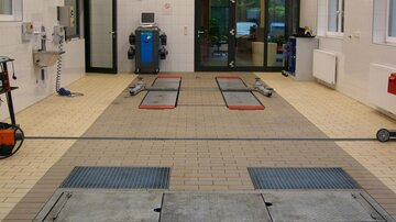 A clean workshop with lifting platforms and a modern workspace. The light is bright and the walls are tiled white.