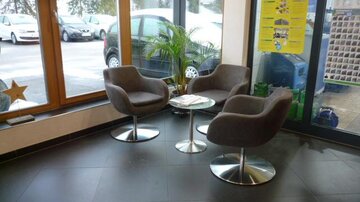 A modern waiting area with two comfortable chairs and a small table. Large windows let in plenty of light and provide a view outside.