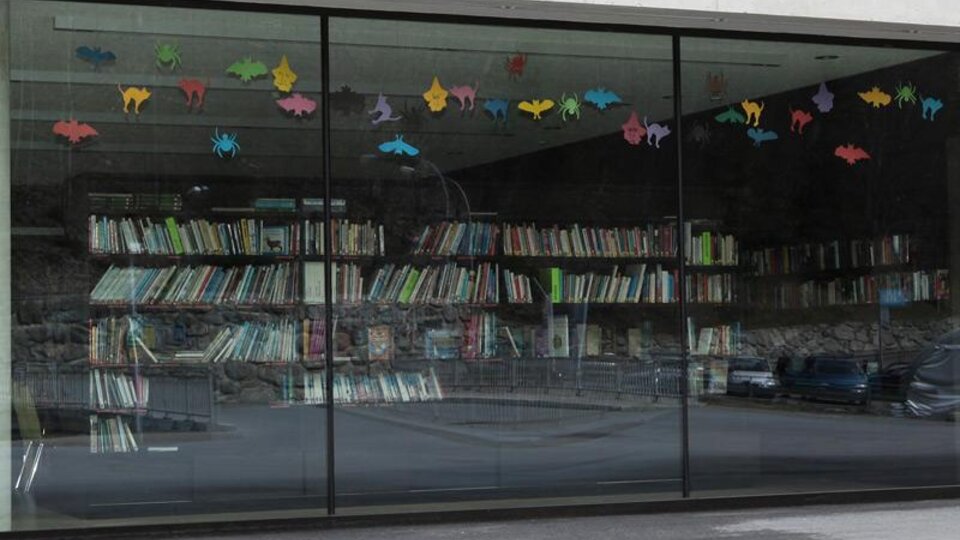 Ein modernes Fenster mit bunten Tiermotiven, das auf eine Bücherwand blickt. Die Bücher sind ordentlich in Regalen angeordnet.