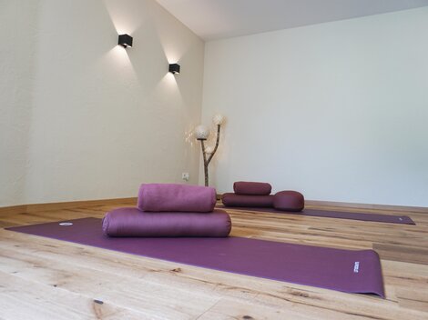 Ein ruhiger Yoga-Raum mit lila Matten liegt auf einem Holzfußboden. Sanftes Licht schafft eine entspannende Atmosphäre.