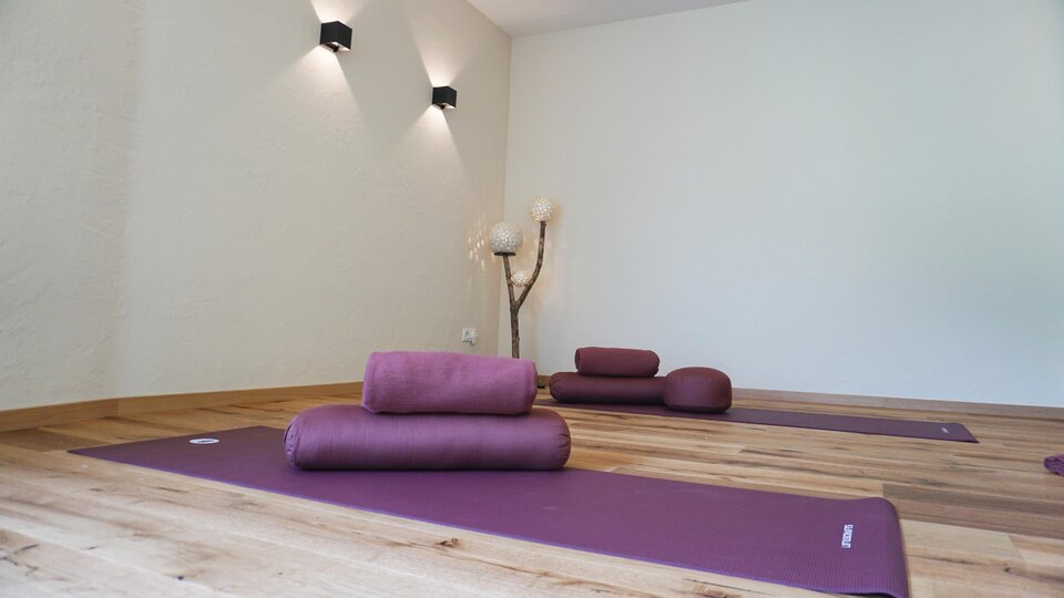 Ein ruhiger Yoga-Raum mit lila Matten liegt auf einem Holzfußboden. Sanftes Licht schafft eine entspannende Atmosphäre.