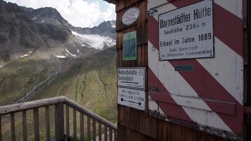 Eine Berghütte mit Sicht auf die umliegenden Berge und Gletscher. Die Hütte hat ein Holzdesign und mehrere informative Schilder.