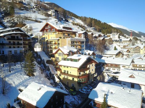 A picturesque winter landscape with snow-covered roofs and traditional wooden buildings. The mountains in the background complete the idyllic scene.