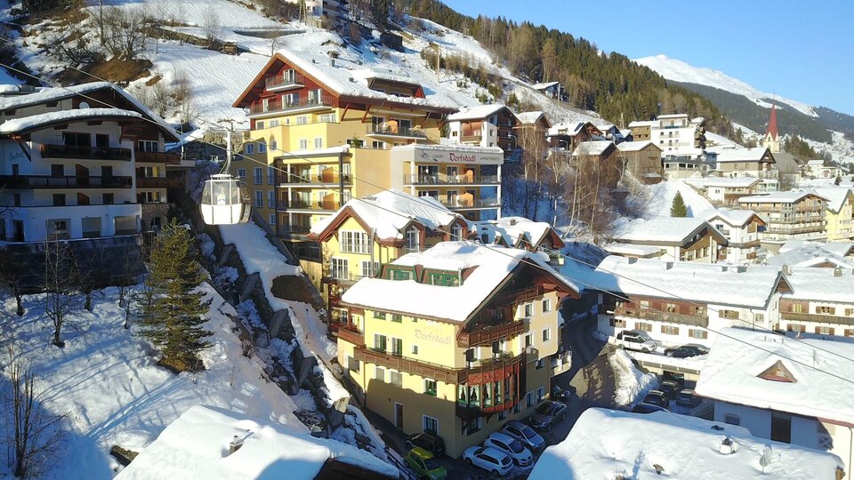 A picturesque winter landscape with snow-covered roofs and traditional wooden buildings. The mountains in the background complete the idyllic scene.
