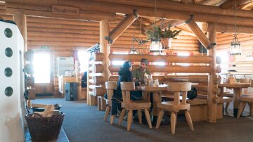 Ein gemütliches Restaurant mit Holzinterieur und rustikalen Tischen. Zwei Personen sitzen zusammen an einem Tisch und genießen ihre Zeit.