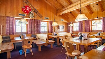 Ein gemütliches Restaurant mit Holzmöbeln und warmem Ambiente. Große Fenster sorgen für viel Tageslicht.