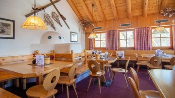 Ein gemütliches Restaurant mit Holzmöbeln und einem rustikalen Ambiente. Die Innenausstattung umfasst große Fenster und dekorative Elemente, die eine einladende Atmosphäre schaffen.