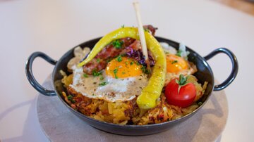 Ein herzhaftes Gericht in einer schwarzen Pfanne mit Spiegelei, knusprigem Speck und Kartoffeln. Mit einer Paprika und einer Kirschtomate garniert.