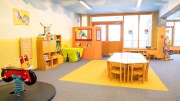 Ein heller und freundlicher Kindergartenraum mit farbenfrohen Möbeln. Es gibt Spielzeuge, Tische und viel Platz zum Spielen.