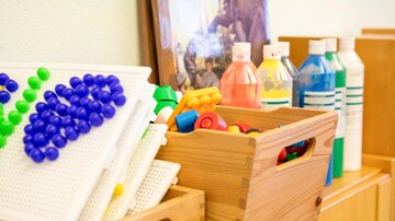 Ein Spielbereich mit bunten Spielzeugen und Materialien. Es gibt Kisten mit Bauklötzen und Flaschen in verschiedenen Farben.