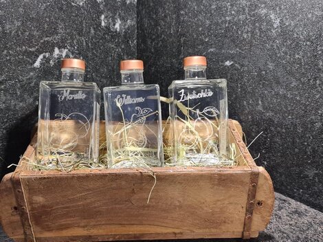 Three glass bottles in a wooden container, surrounded by hay. The bottles are sealed with corks and labeled.