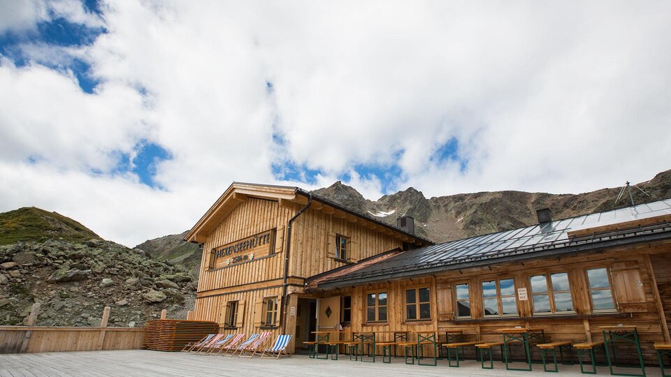 Ein rustikales Holzhaus in den Bergen mit großen Fenstern. Der Himmel ist bewölkt und die Umgebung ist natürlich und grün.