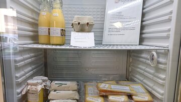 Ein Kühlschrank mit verschiedenen Lebensmitteln, darunter Flaschen mit Getränken, Eier und mehrere verpackte Lebensmittel. Auf der oberen Etage befindet sich ein Schild mit Informationen.