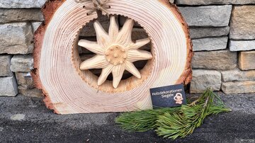 Ein Holzschild mit einem geschnitzten Stern und einer natürlichen Holzoberfläche. Daneben liegen frische Nadelzweige und eine kleine Karte.