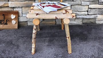 Ein rustikaler Stuhl aus Holzstämmen steht vor einer steinernen Wand. Auf dem Stuhl liegen einige Magazine.