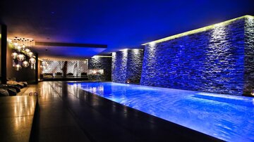 Ein eleganter Innenpool in einem gedimmten Raum, beleuchtet von blauen Lichtern. Die Wände sind mit modernen Steinelementen gestaltet, was eine entspannende Atmosphäre schafft.
