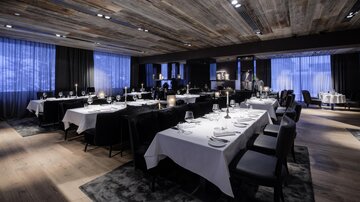 Ein elegantes Restaurant mit stilvoll gedeckten Tischen und modernem Ambiente. Die Beleuchtung und die Fenster sorgen für eine gemütliche Atmosphäre.
