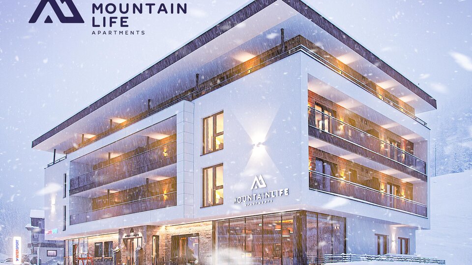 Ein modernes Apartmentgebäude im Schnee, umgeben von einer winterlichen Landschaft. Die Fassade ist in hellen Tönen gehalten und verfügt über große Fenster.
