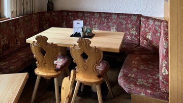 Ein gemütliches Restaurant mit Holzdekor und einer Fernsehecke, die ein Sportspiel zeigt. Am Tisch sitzen dekorative Stühle und das Ambiente ist einladend.