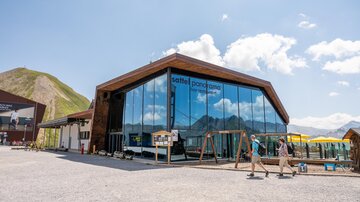 Ein modernes Gebäude mit großen Fensterflächen in den Bergen. Vor dem Gebäude sind Freizeitmöglichkeiten und eine klare Sicht auf die Umgebung.