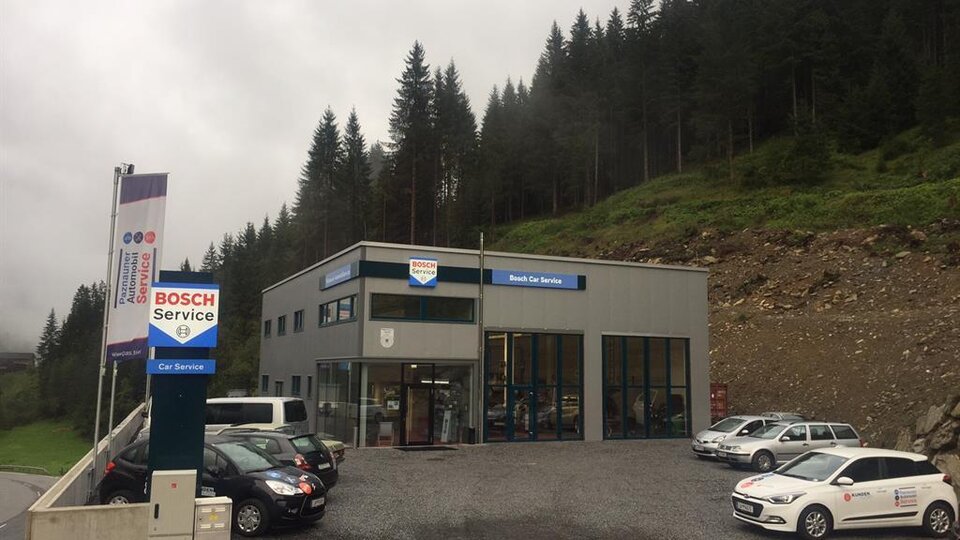 Ein modernes Servicegebäude von Bosch, umgeben von Wälder und Bergen. Auf dem Parkplatz stehen mehrere Autos.