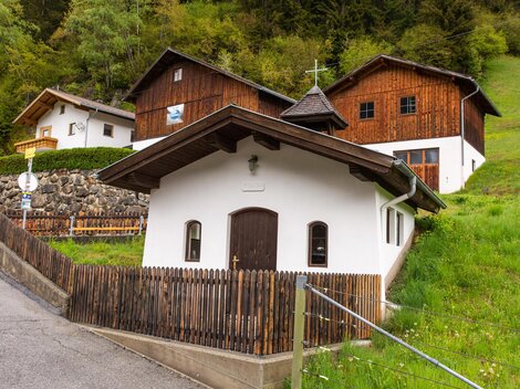 Ein malerisches Dorf mit traditionellen Holzhäusern und einer kleinen Kirche. Umgeben von grünen Wiesen und Bäumen. | © Bernhard Gruber – Photography