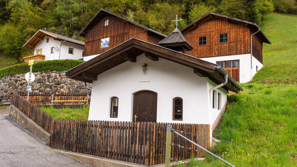 Ein malerisches Dorf mit traditionellen Holzhäusern und einer kleinen Kirche. Umgeben von grünen Wiesen und Bäumen. | © Bernhard Gruber – Photography