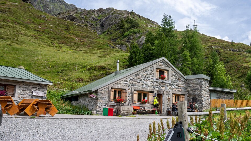 Ein gemütliches Steinhaus in einer malerischen Berglandschaft. Umgeben von grünen Wiesen und Bergen ist es ein idyllischer Rückzugsort.