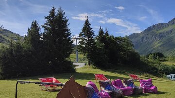 Ein schöner Außenbereich mit Liegestühlen und einem Schild der Bike Arena. Die umgebende Landschaft ist grün und bergig unter einem klaren blauen Himmel.